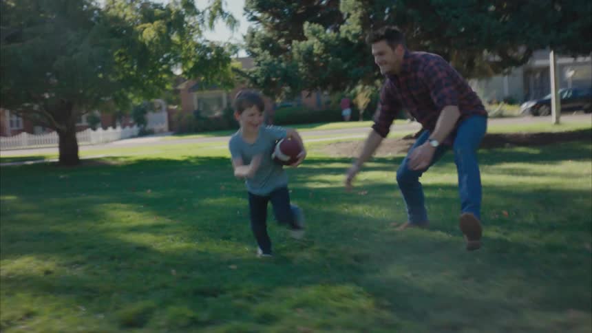 A boy and his father playing american football in a public park