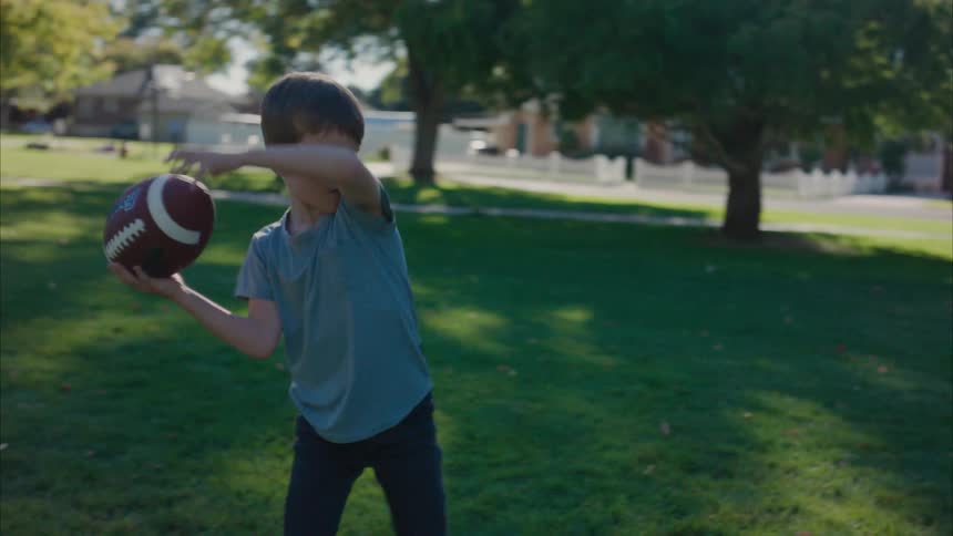 A little boy is playing in his yard as he throws a football