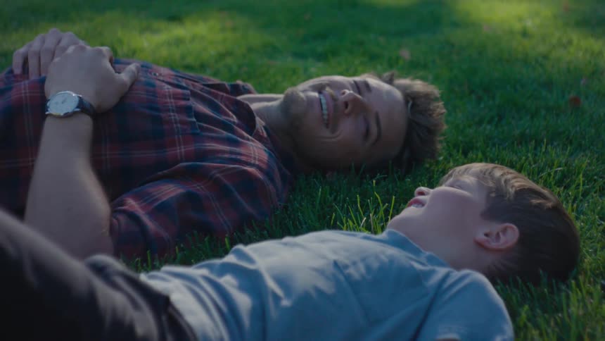 Father and son fist bump while laying on the grass talking at midday