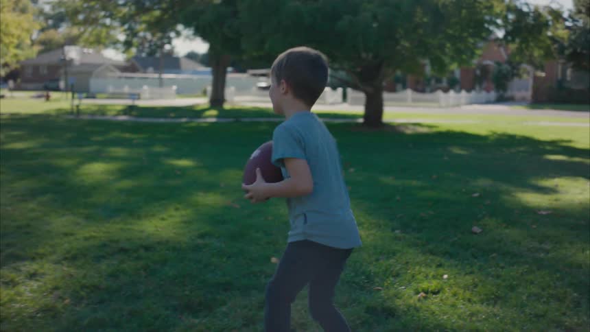 A little boy is playing catch with his father on a lawn