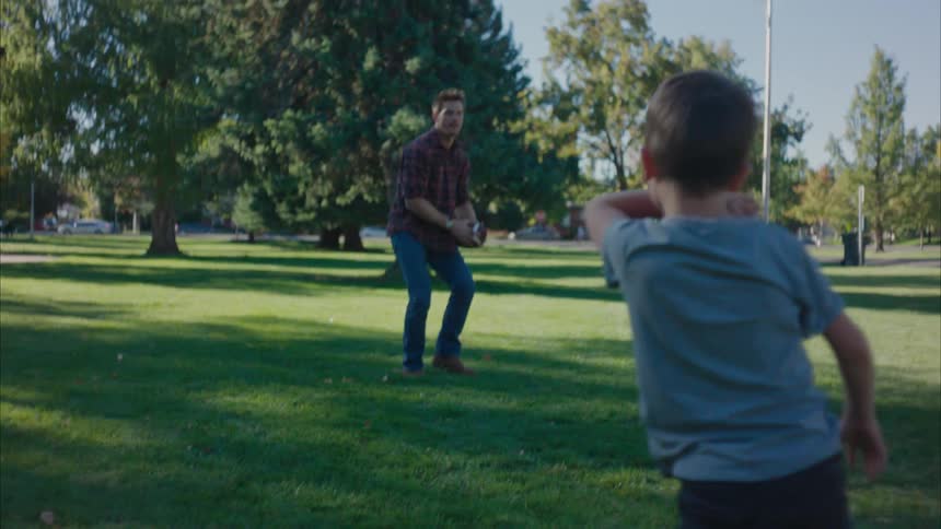 A boy and his father play american football in a public park