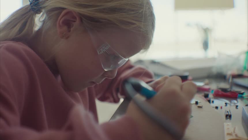 Blonde girl concentrates on soldering circuit board at home