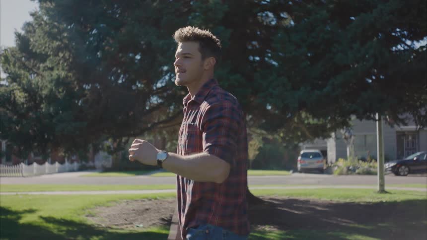A man catches a football and throws it back while the sun shines down and glares from between the trees in a neighborhood park in the suburbs