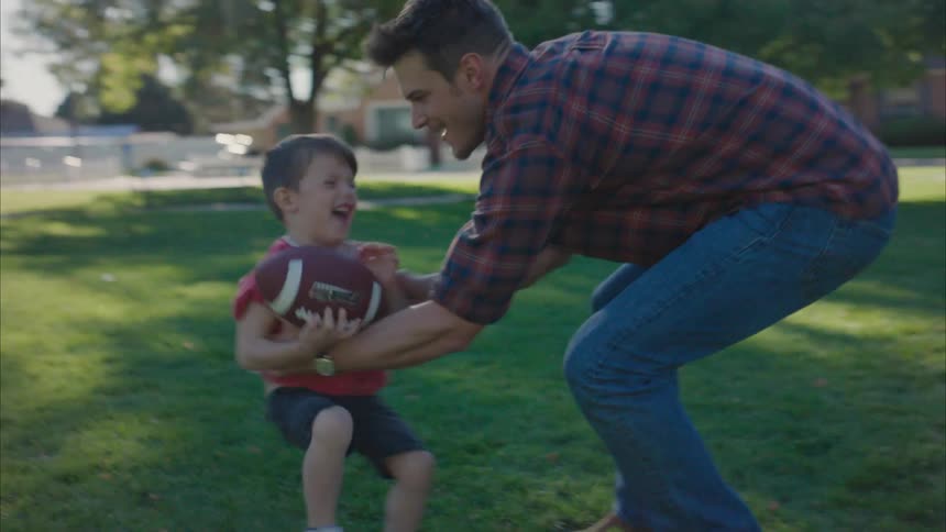 A father picks up his son as they play american football in a public park