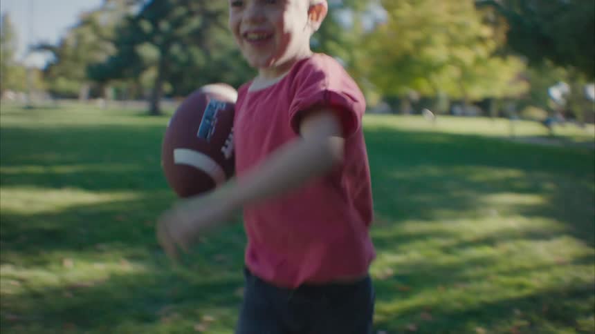 A boy running happily with a ball in his hand and an adult picks him up