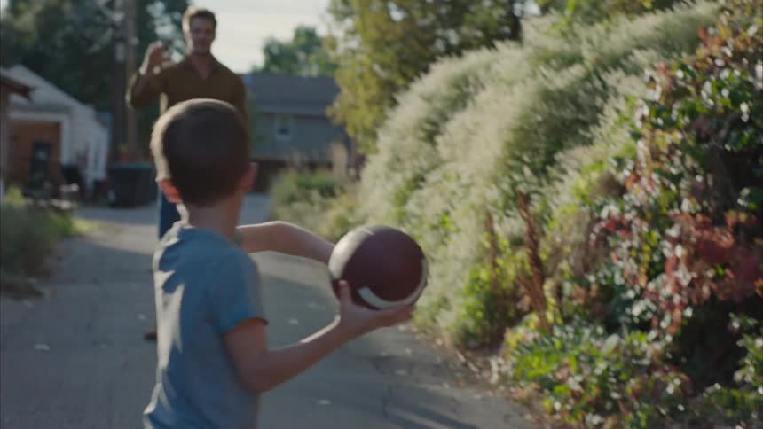 A little boy playing with an american football to his father
