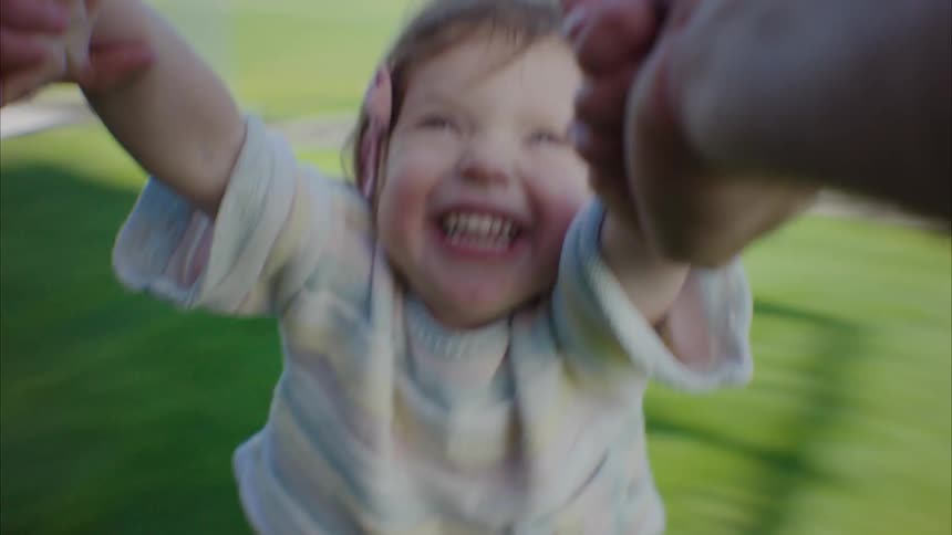 Child smiles as father spins her around himself by the arms on the lawn on their home