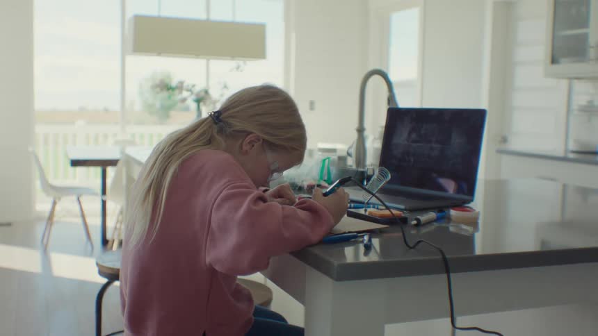 A young girl working with a soldering iron on a table in front of a laptop