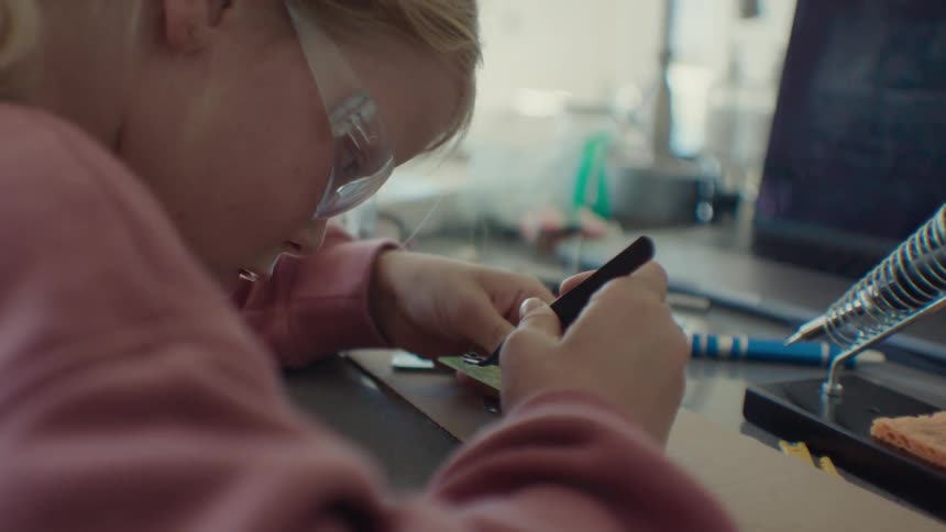 A girl with electronic parts on a table with a laptop