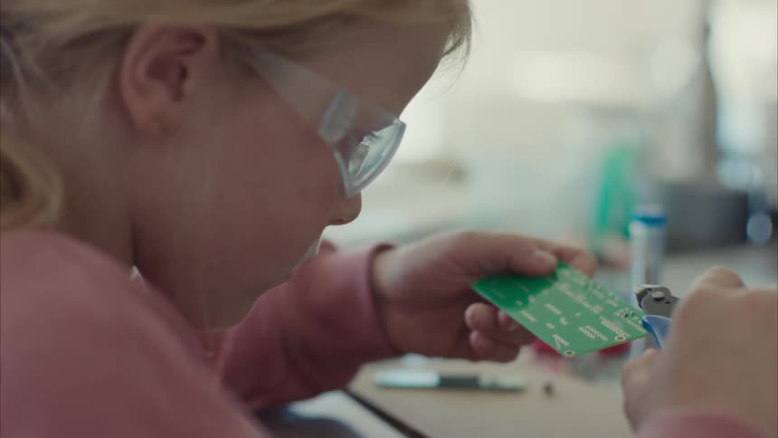 Female child working on a circuit board while seated indoor at midday