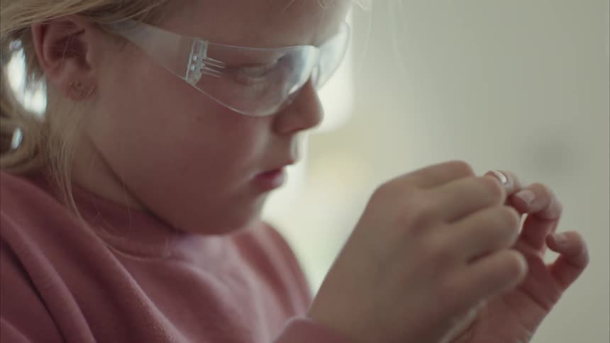 A little girl wearing transparent glasses to see something in her hands