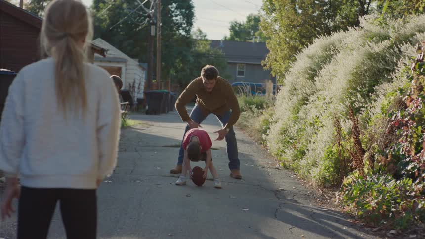 Father playing with his children on a narrow street with an american football