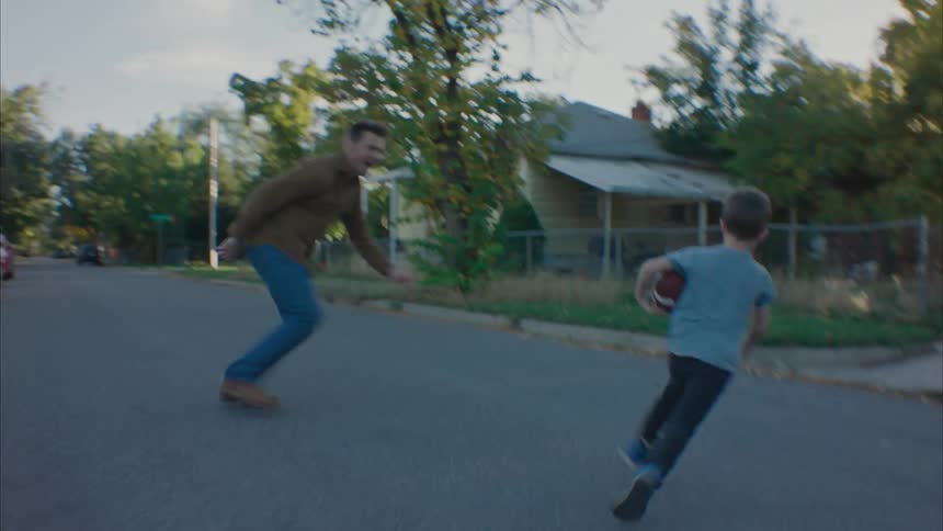 Child running and his father picking him up in play in the middle of a residential neighborhood street