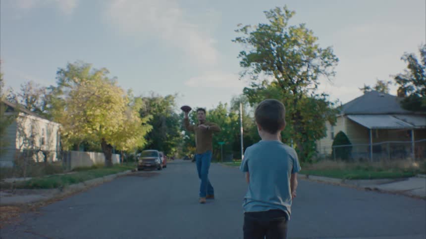 A man plays football with his kids in middle of the road in quiet neighborhood