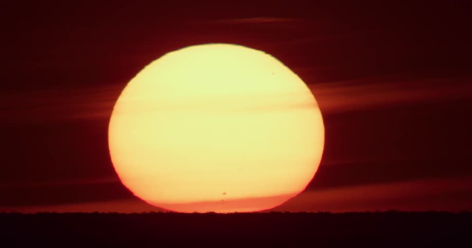 A big yellow sun sets on the horizon in a deep red sky