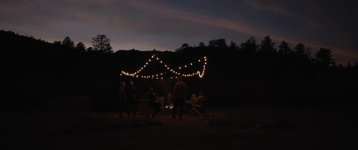 Friends around a campfire have a small party outdoors at sunset