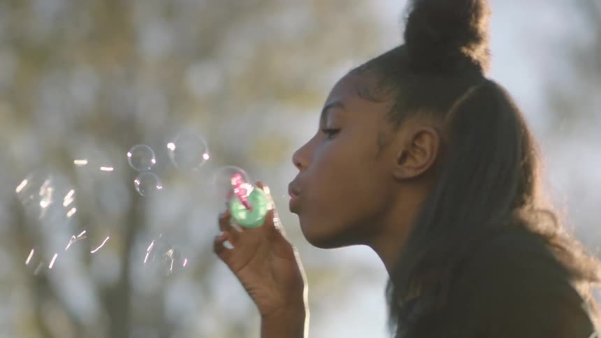 A black teenage girl blowing bubbles in the air