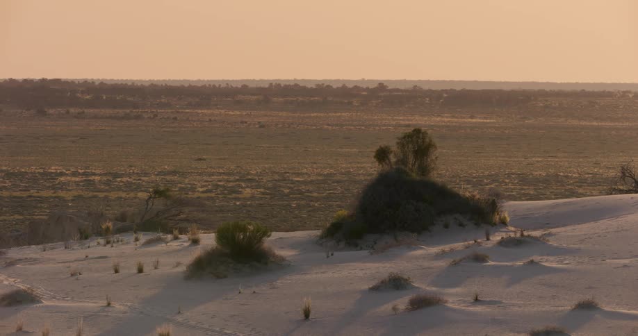 Sunset in a side barren dessert landscape beyond a white sand slope