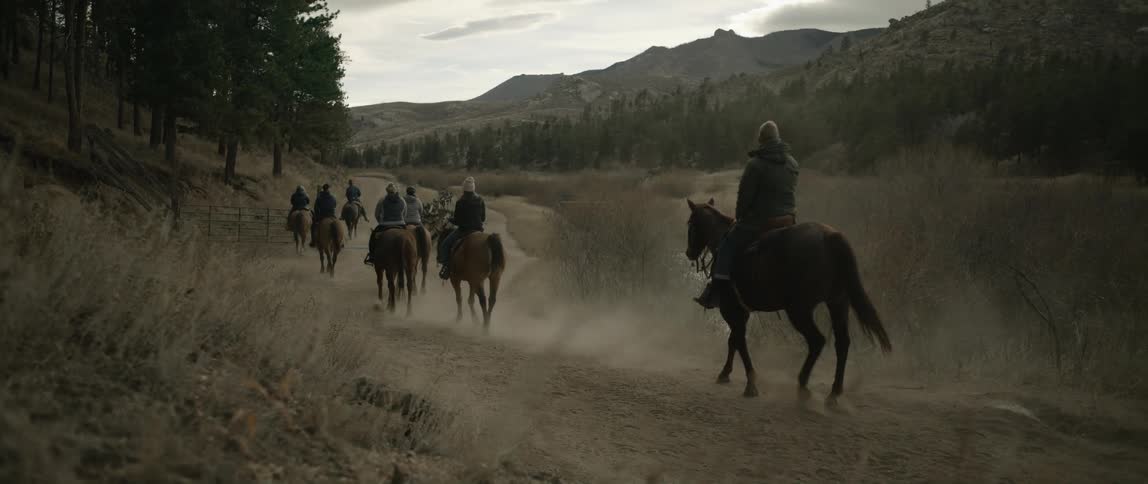 People riding horses on a trail amid a natural setting with mountains and forests