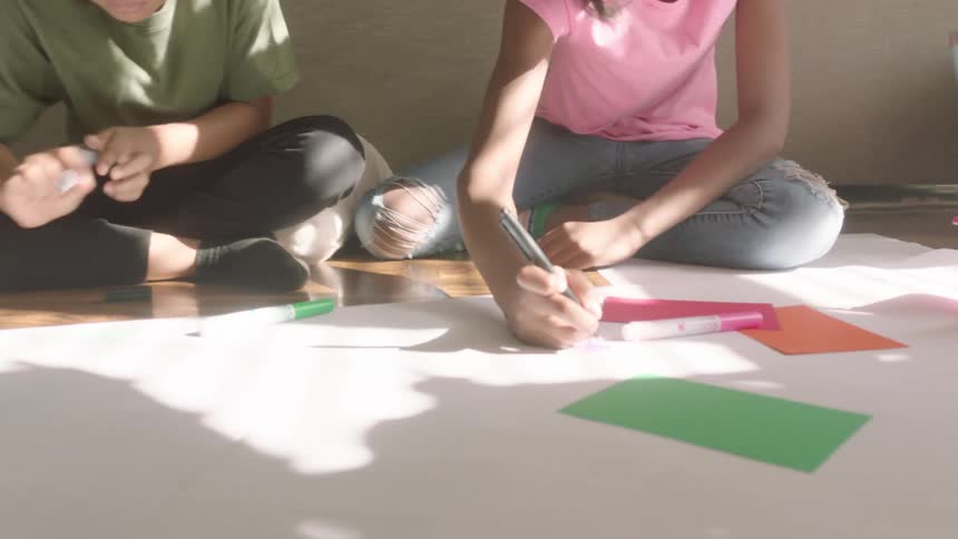 Siblings sitting on the living room floor drawing on white poster boards