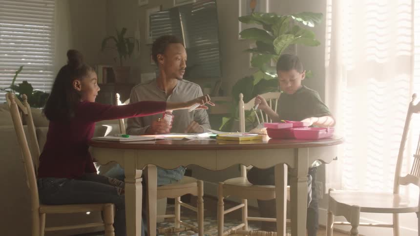 Father sitting with his children at the table helping with school tasks