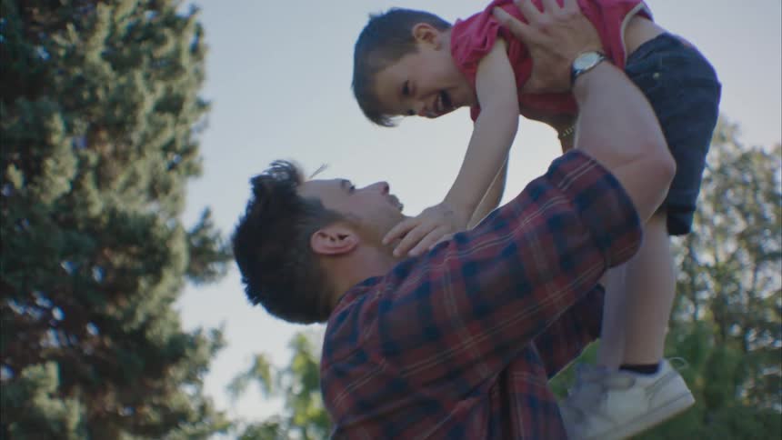 Father carries son in the air in a park and both smile
