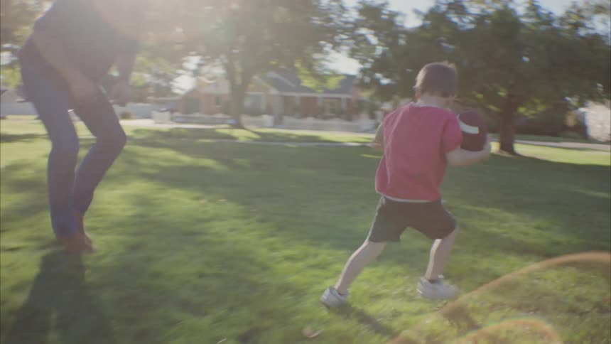 Child running from their father while holding a football