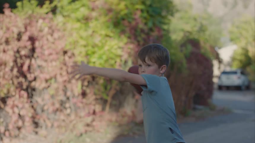 A little boy is throwing an american football