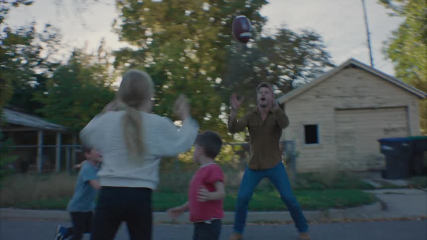 Father throwing the american football to his daughter with his other two boys trying to catch the ball
