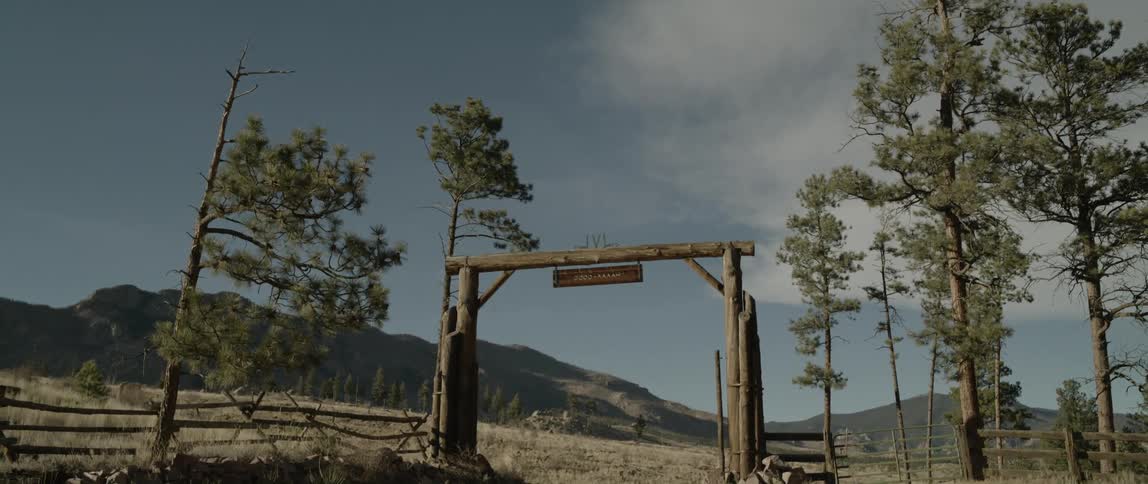 Landscape of an entrance with a wooden fence in a natural setting with fields and mountains around