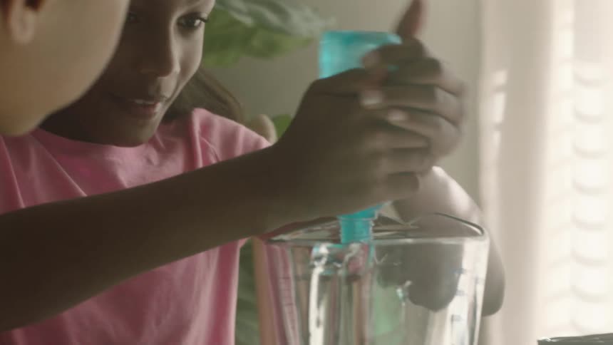 A girl squeezing blue slime into a glass jar