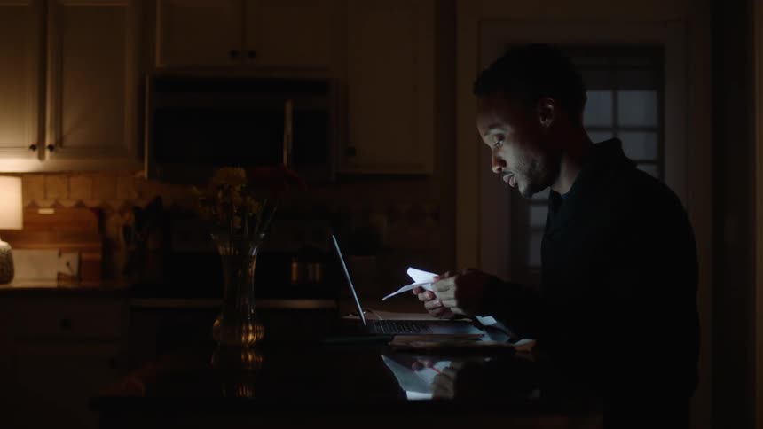 A man looks worried while looking at papers and then moves on a laptop in front of him