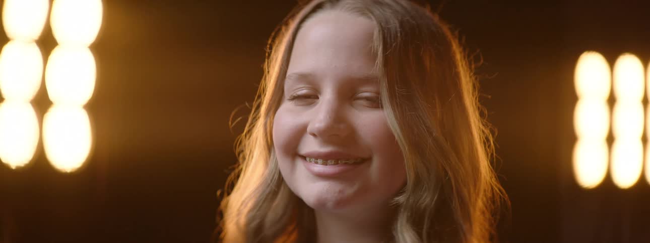 A young girl with a smile on her face with yellow lamps illuminating her