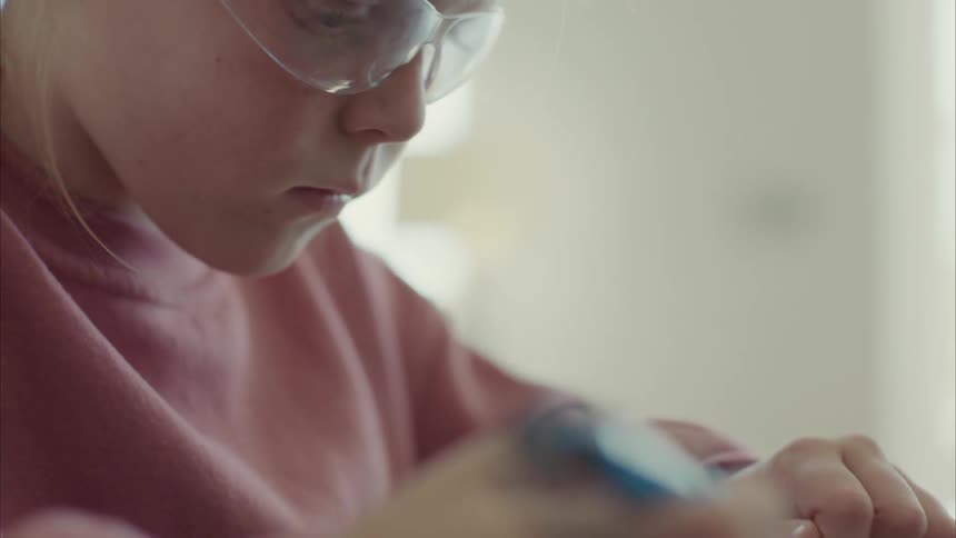 Female child using soldering iron while seated indoor at midday