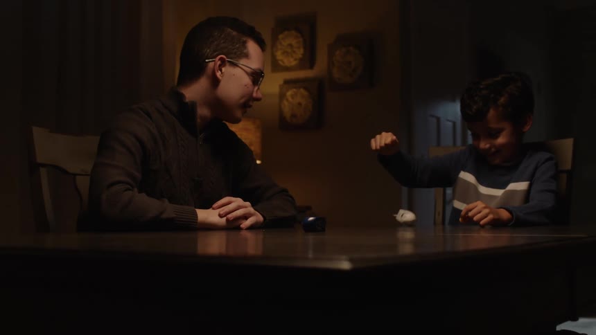 A man wearing glasses playing with his child while sitting on the table