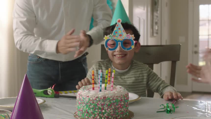 Child blows off cake candles while the parents claps in celebration