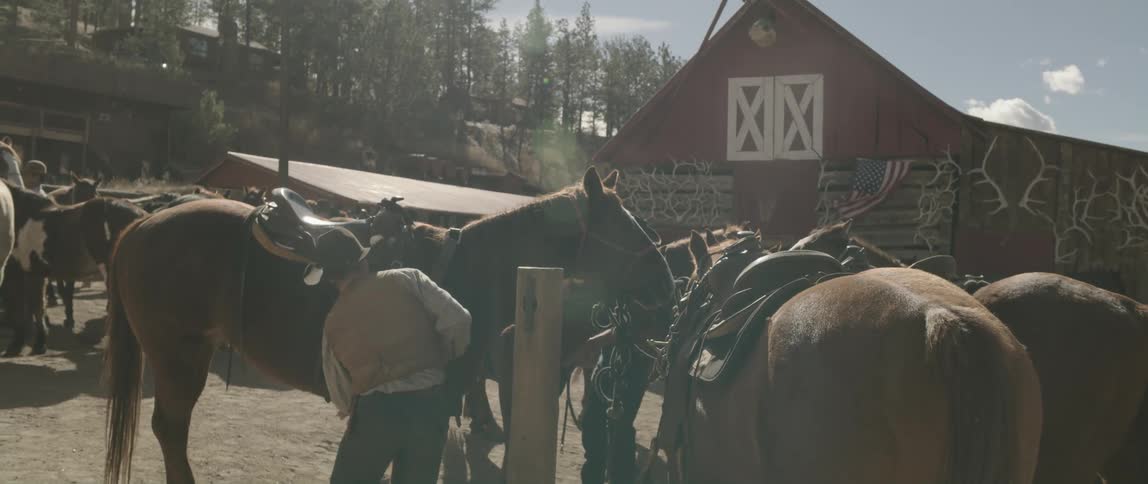 Cowboy tending to horses next to a barn