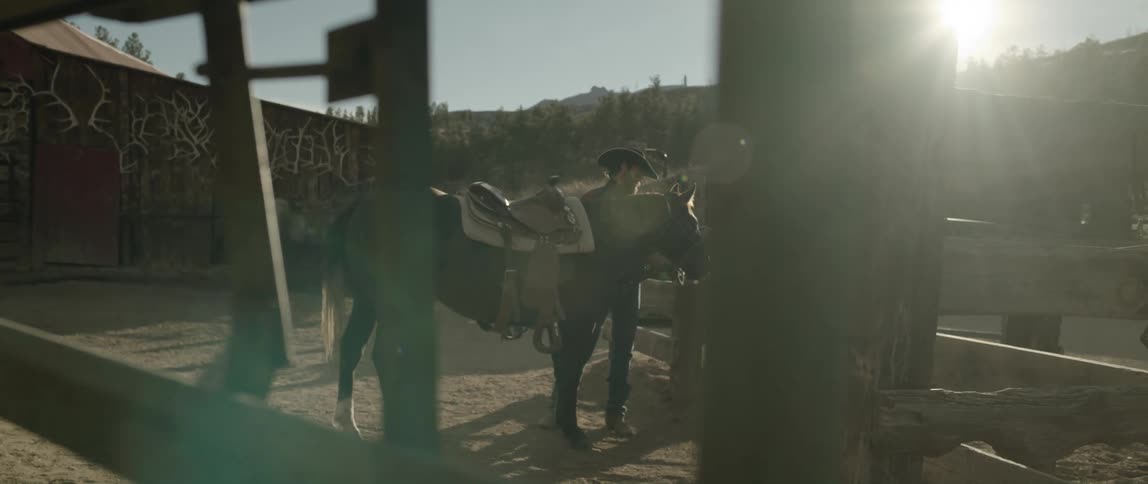 Cowboy readies horses saddle while standing in corral on sunny day