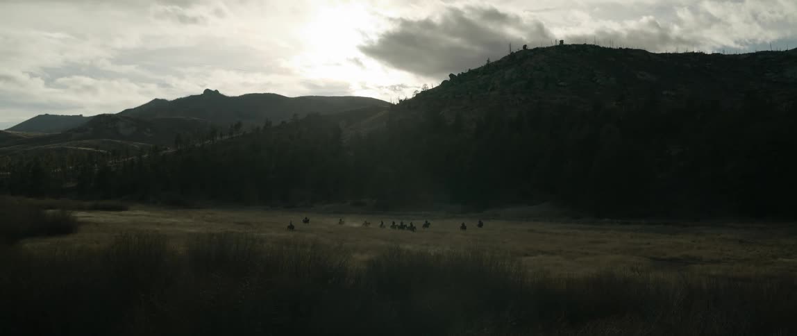 Panorama of a landscape amidst mountains and fields with horses on the horizon
