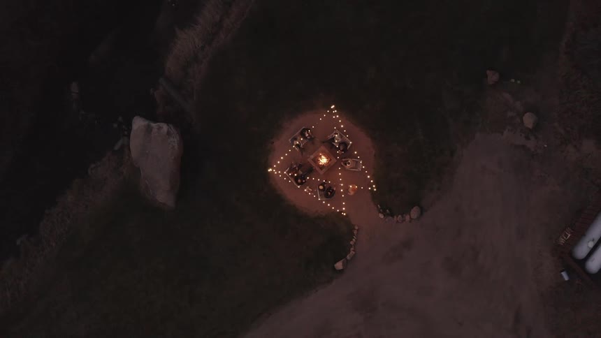 People sit around firepit under a string of lights at night