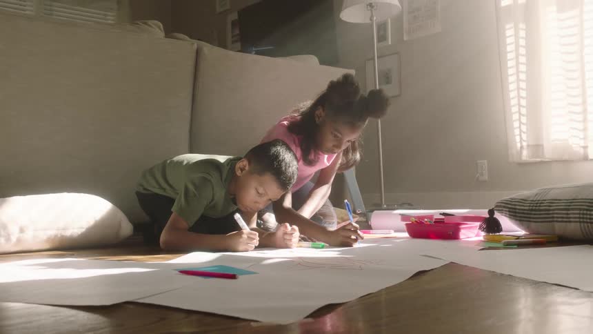 Siblings drawing on the living room floor