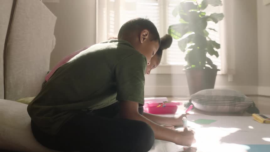 Boy and girl sitting on the floor drawing on poster boards