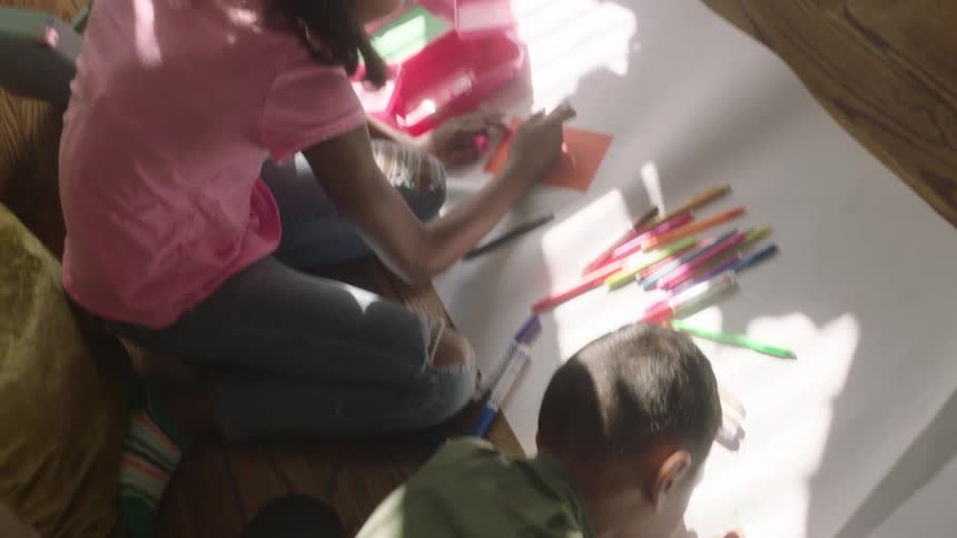 Two girls writing with different colors on a large white cardboard paper