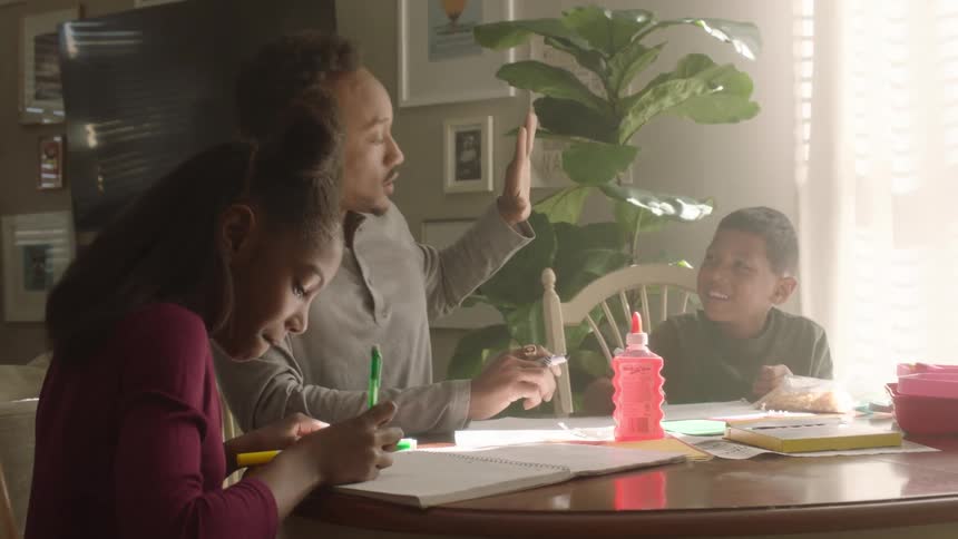 Father sitting at the table with his children drawing and holding hands with the boy