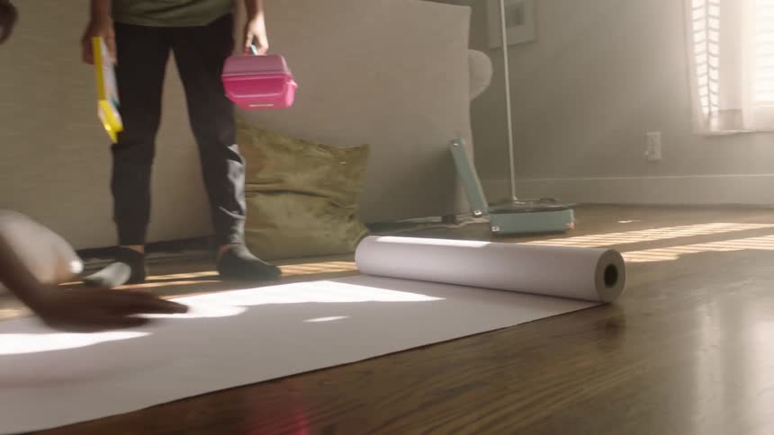 Lady rolled a long paper on the floor indoor while a man stands to watch