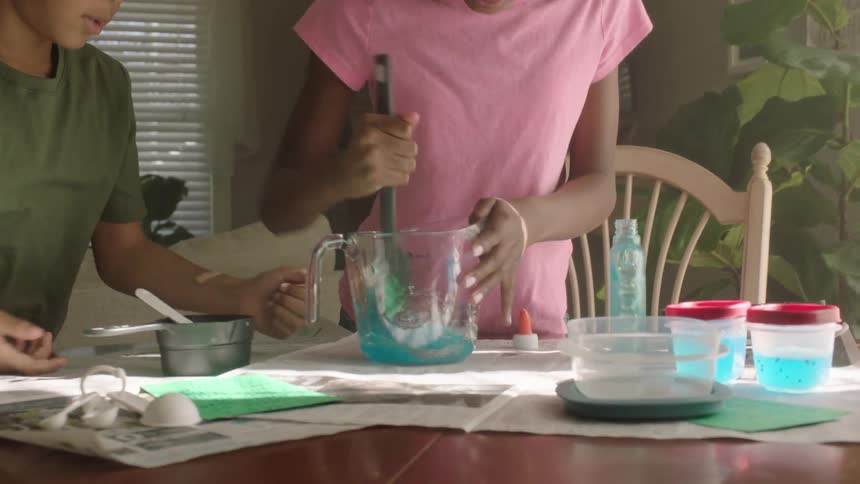 Two children making blue slime on the table in a container