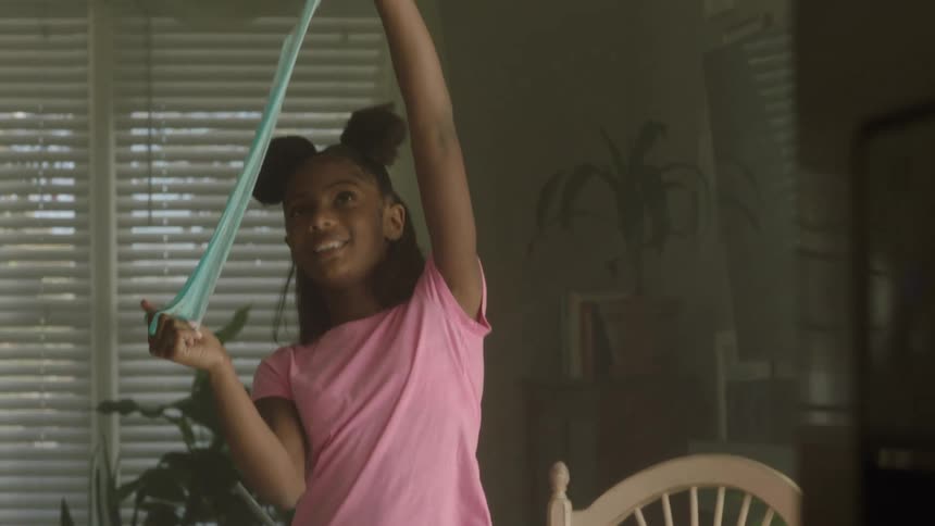 A girl is playing with green slime that she made in her dining room