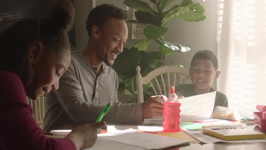 Father sitting at the table with his children all smiling and writing and drawing
