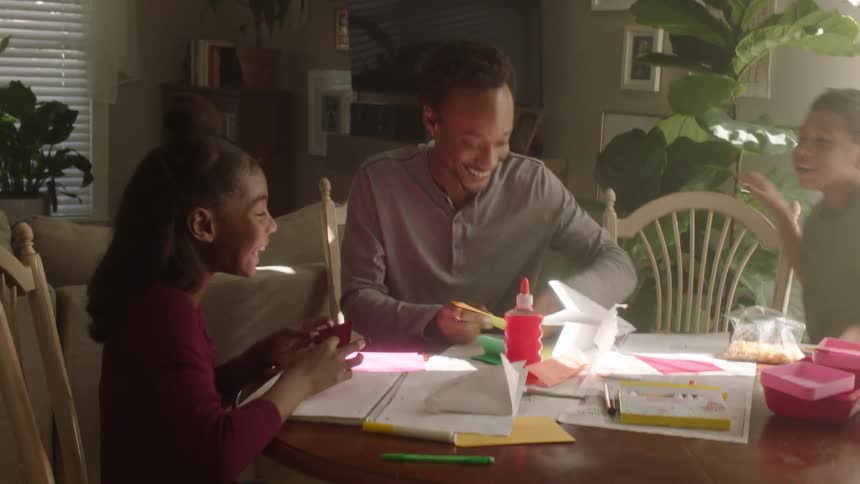 Father sitting at the table with his children while they play and engage in paper activities