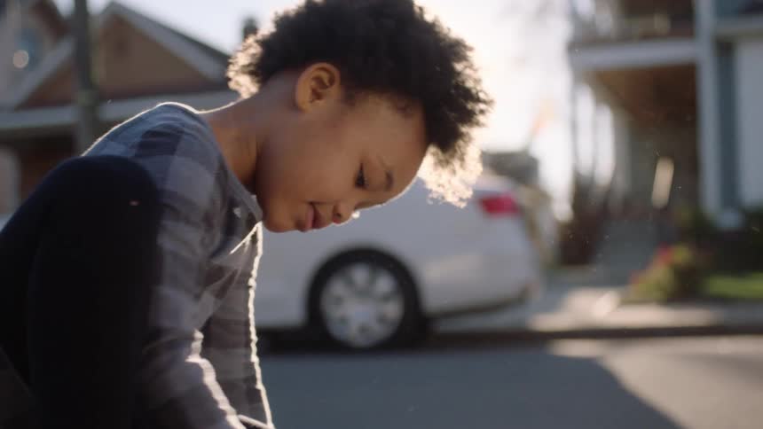 A child in the middle of the street on a sunny day writing on the road with colors